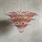 Pink glass Palmette chandelier shown in a wider studio view on a gray wall.